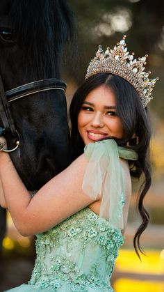 a beautiful young woman in a green dress hugging a black horse