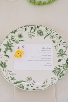 a yellow flower on a white and green plate with a card in it's center