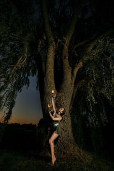 a woman standing in front of a tree at night holding an object up to her face