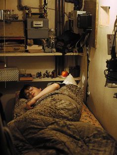 a woman laying on top of a bed in a room filled with shelves and equipment