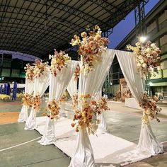 an outdoor ceremony setup with white drapes and floral arrangements on the sidelines at night