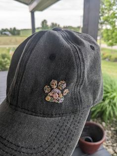 a gray hat with an embroidered flower on the front, and a small potted plant behind it