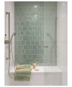 a bathtub with green tile and towels on the edge, next to a shower head