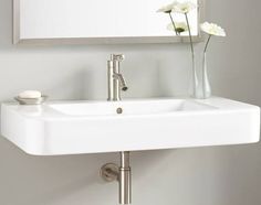 a white sink sitting under a bathroom mirror next to a vase with flowers in it