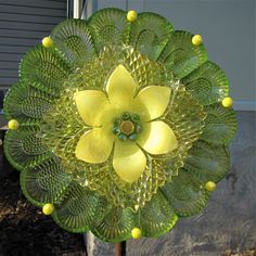 a green glass flower sitting on top of a metal pole in front of a house