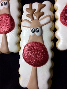 three decorated cookies with reindeer faces and red glitters on them, sitting next to each other