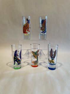 four shot glasses with different designs and colors on the glass are lined up against a white background