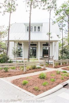 a white house with lots of trees and plants around it's front yard area