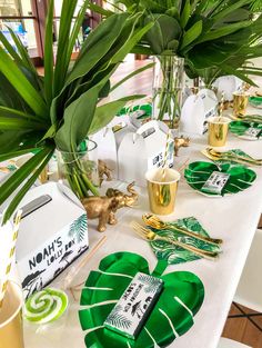 the table is set with gold and green plates, silverware, napkins, and palm leaves