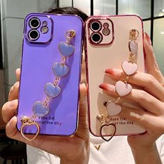 two women holding up their cell phones with heart shaped charms attached to the back of them