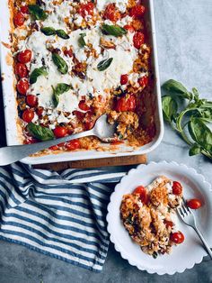 a casserole dish with tomatoes, cheese and spinach leaves on the side