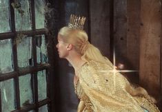 a woman in a golden dress with a crown on her head looking out the window