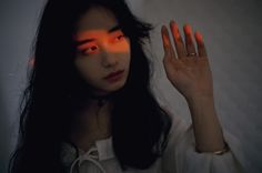 a woman holding her hand up in the air with an orange light shining on her face