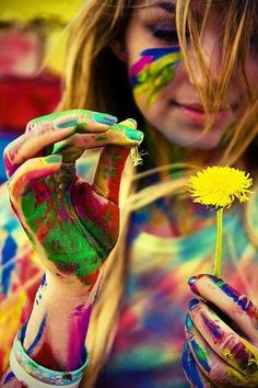 a woman with her hands painted in different colors and holding a yellow dandelion