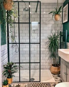 a bathroom with green walls and white tiles on the shower wall, plants in potted planters next to the bathtub