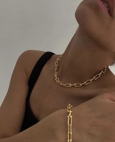 a woman wearing a gold chain necklace and black tank top with her hands on her chest