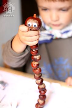 a young boy holding up a bead sculpture with googly eyes and an apple on it