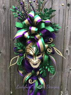 a mardi gras mask with green and purple ribbons hanging on a wooden fence