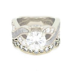 a white gold and diamond ring with an intricate design on the center, surrounded by round brilliant cut diamonds