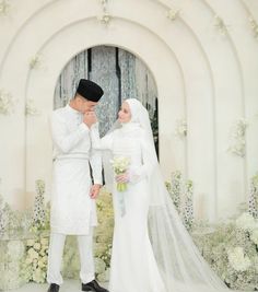 a man and woman standing next to each other in front of a white arch with flowers