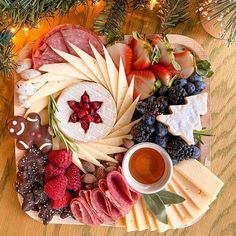 an assortment of cheeses, fruits and meats arranged on a platter next to a christmas tree