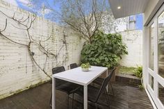 a white table and chairs on a wooden floor in front of a brick wall with trees