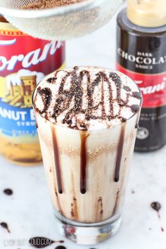 an iced drink with whipped cream and chocolate toppings on the top, next to two cans of cocoa