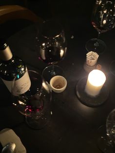 a table topped with wine glasses next to a bottle of wine and a lit candle