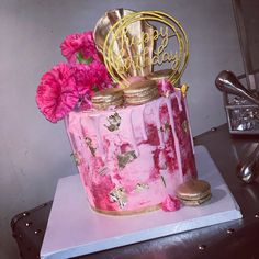 a pink and gold birthday cake sitting on top of a table