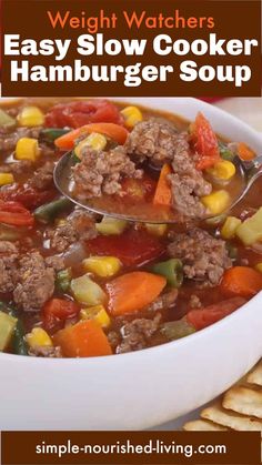 a bowl of hamburger soup with a spoon in it and crackers on the side