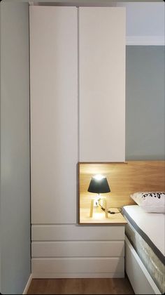 a bedroom with a bed, lamp and white cupboards on the wall next to it