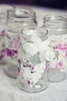 four glass jars filled with white and pink flowers on a table cloth covered tablecloth