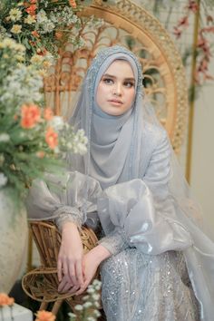 a woman wearing a veil and sitting on a chair with flowers in the back ground