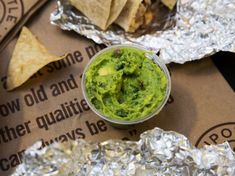 a bowl of guacamole sitting on top of foil wrappers next to some tortilla chips