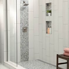 a walk in shower with tiled walls and white tiles on the wall next to a wooden stool