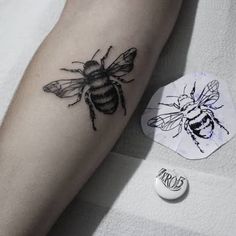 a black and white photo of a bee tattoo on the left arm, next to a button