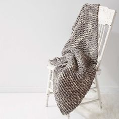 a white rocking chair with a knitted blanket on it's back next to a white wall