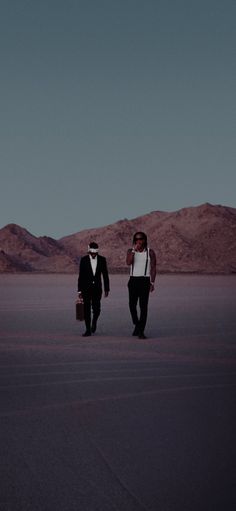 two men in tuxedos are walking through the desert