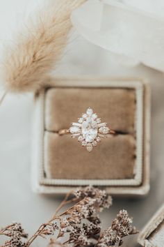 an engagement ring sitting on top of a box next to some dried flowers and feathers