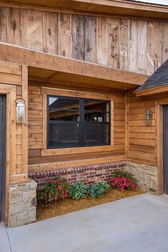 a wooden building with two garage doors and flowers in the front garden bed on the sidewalk