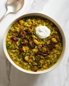 a white bowl filled with beans and other food on top of a marble table next to a spoon