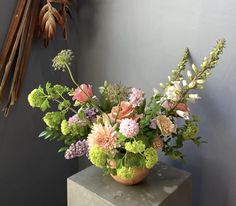 a vase filled with lots of flowers sitting on top of a cement block next to a wall