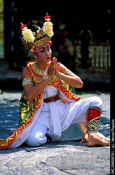 a woman dressed in traditional thai garb sitting on the ground with her hands clasped