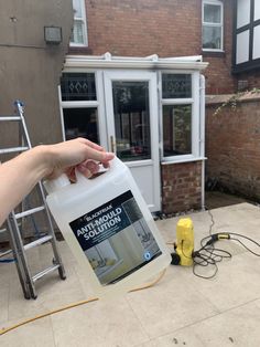 a hand holding a gallon of cleaning solution in front of a brick building with a yellow fire hydrant