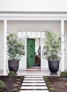 two large black planters sitting in front of a green door on a white house