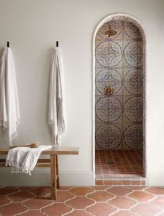 two white towels hanging on the wall next to a wooden bench and tiled flooring