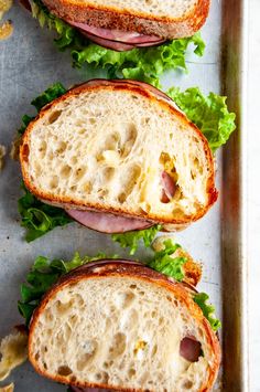 three sandwiches with meat, cheese and lettuce sitting on a tray next to chips