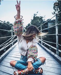 a woman sitting on top of a wooden bridge with her hands up in the air