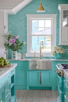 a kitchen with blue cabinets and white counter tops, along with flowers in a vase on the window sill