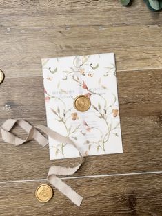 the wedding card is next to two gold coins on a wooden table with greenery